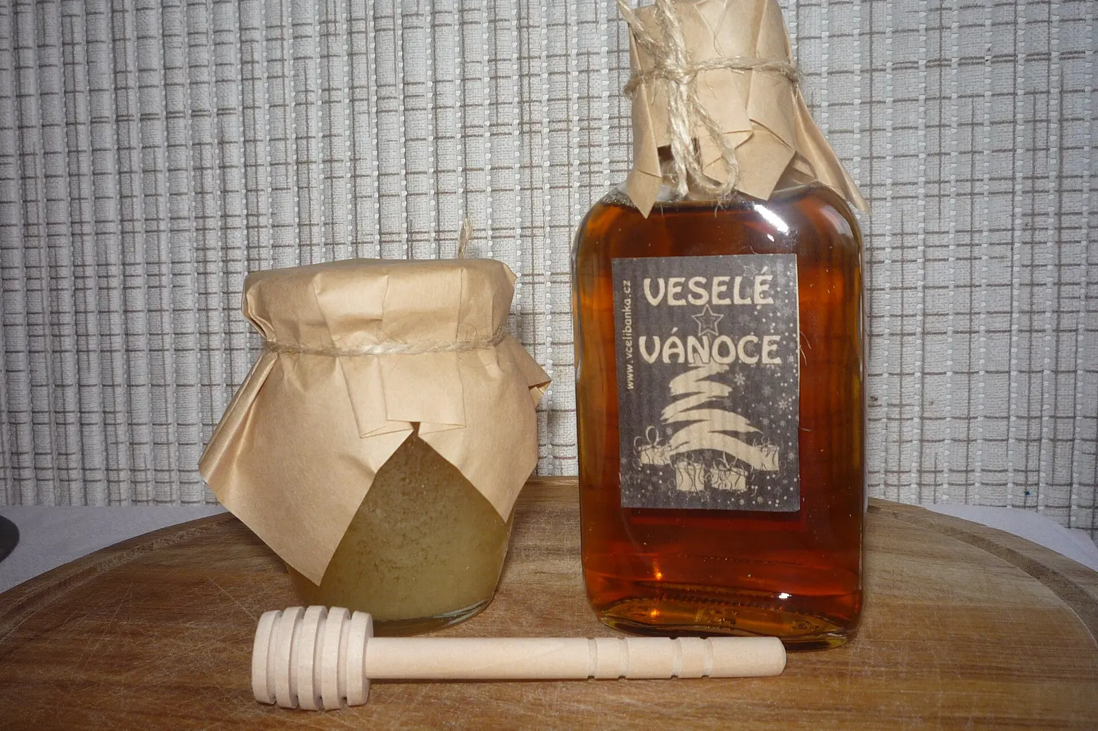 A jar of honey with a wooden dipper beside a glass bottle of amber medovina, the Czech word for mead