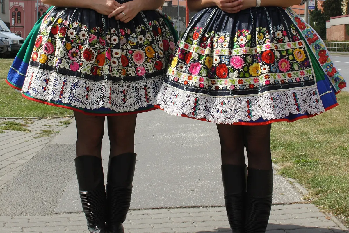 Two young women in Slovácko costume with full skirts embroidered in bright flowers, white puffed sleeves, red vests and tall black boots